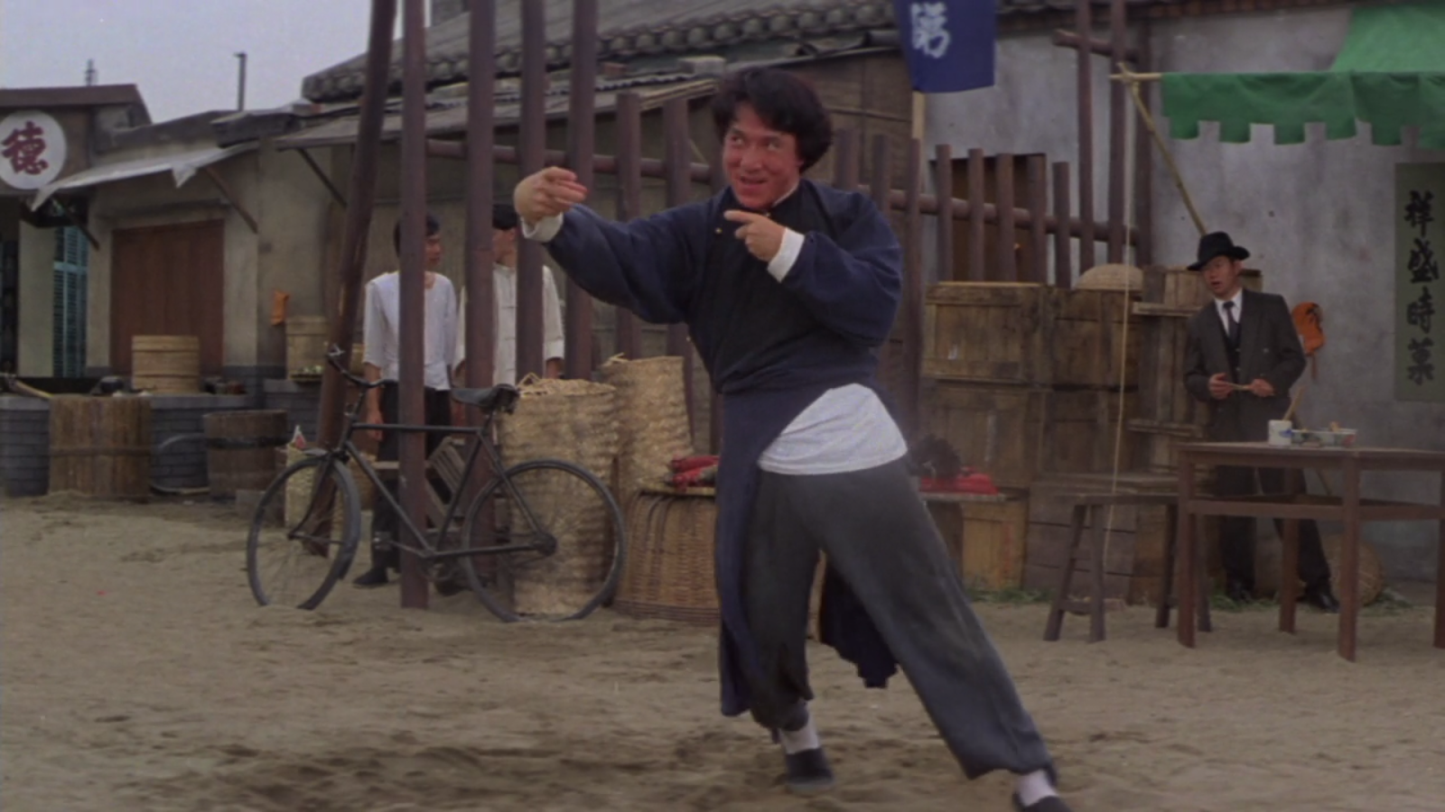 Jackie Chand doing a drunken boxing pose in a marketplace.