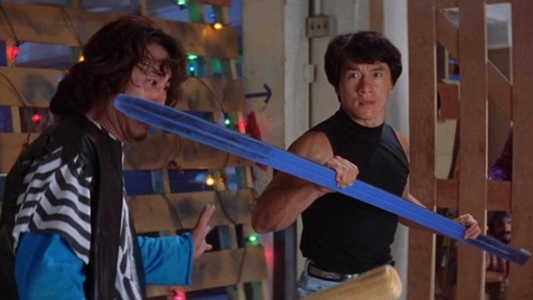 Jackie Chan from Rumble in the Bronx, fighting with another man. He's holding a blue ski with its tip against the cheek of the man he's fighting.