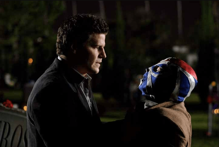 Angel holding Number Five by the collar, shot from the side. Number Five wears a Luchadore mask, blue and red.