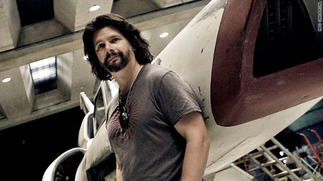 A promotional Image of Ron Moore leaning against a Viper starfighter