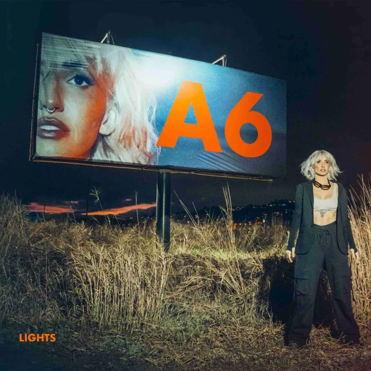 The album cover for Lights' A6. Lights stands in the bottom right, a billboard of her face next to A6 behind her.