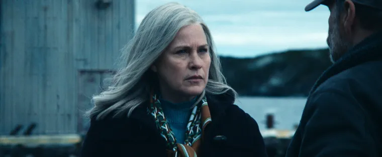 A shot from Severance. Harmony Cobel stands outside in the center of the screen, talking to a man. A decaying building and far away hills are in the background.